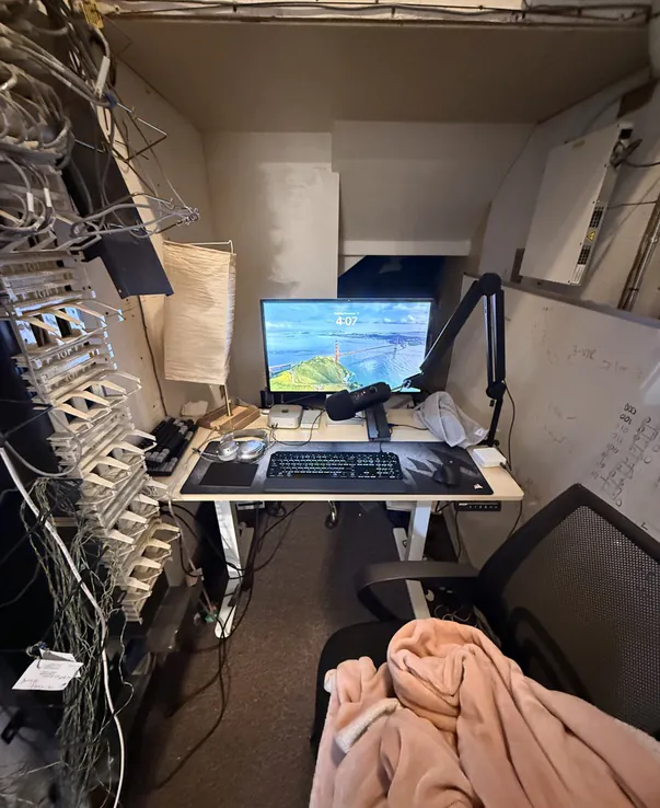A desk with a monitor in a closet under the stairs, cables along the wall